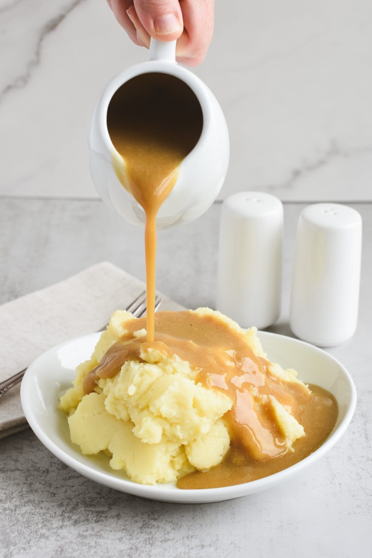 Pouring gravy onto a plate of mashed potatoes.