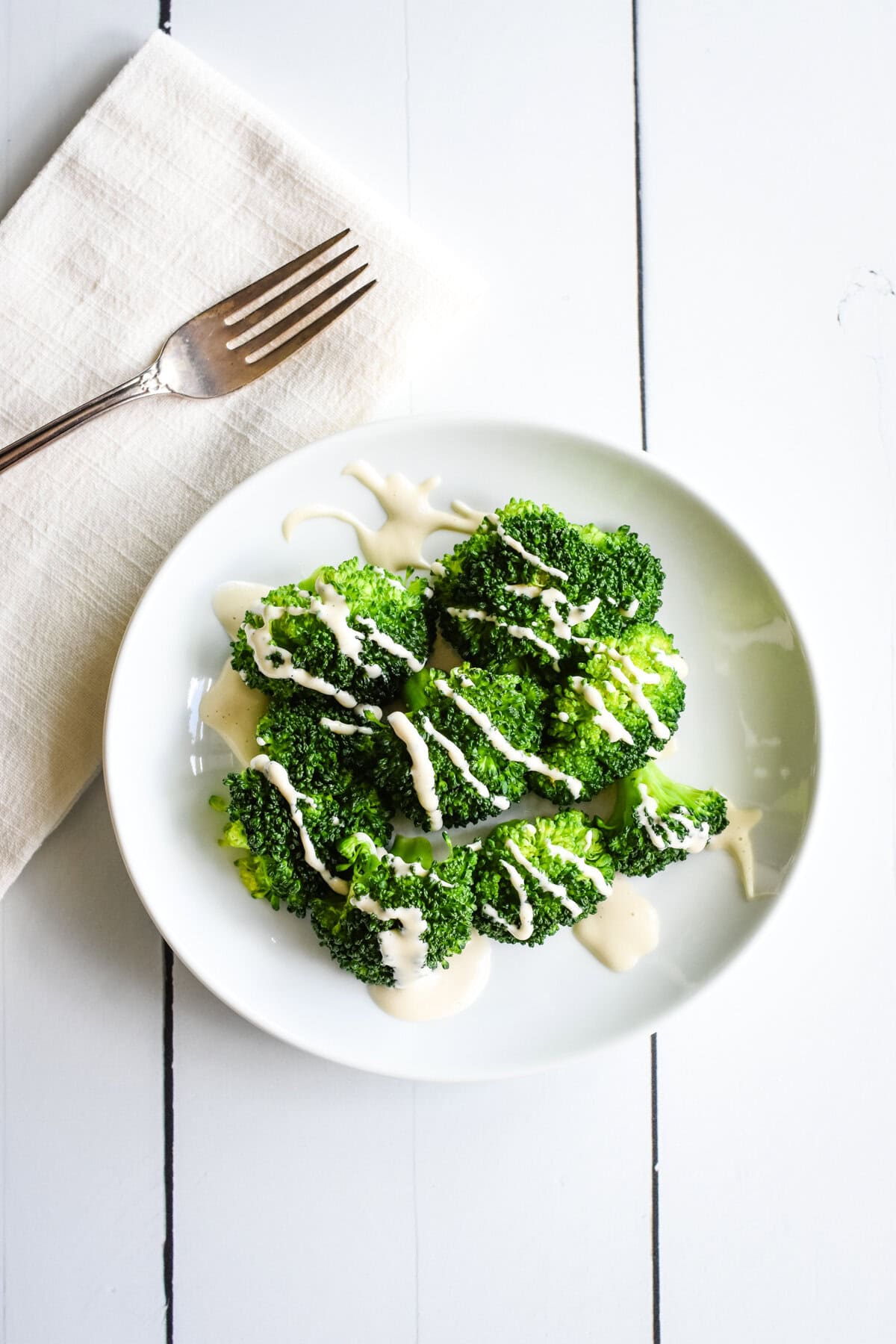 A white plate with a serving of steamed broccoli and cashew mozzarella sauce.