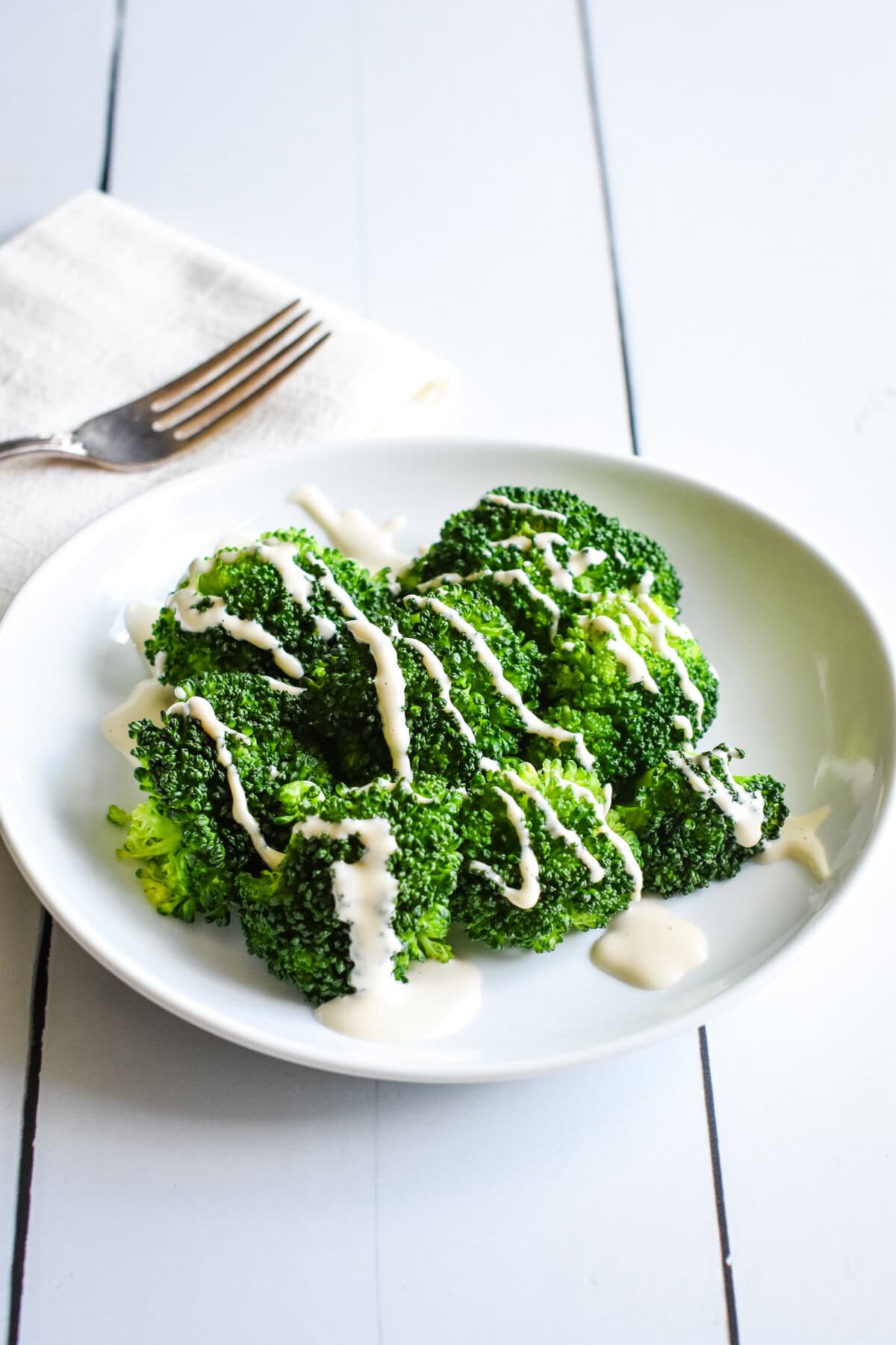 Steamed broccoli on a white plate with non-dairy mozzarella sauce.