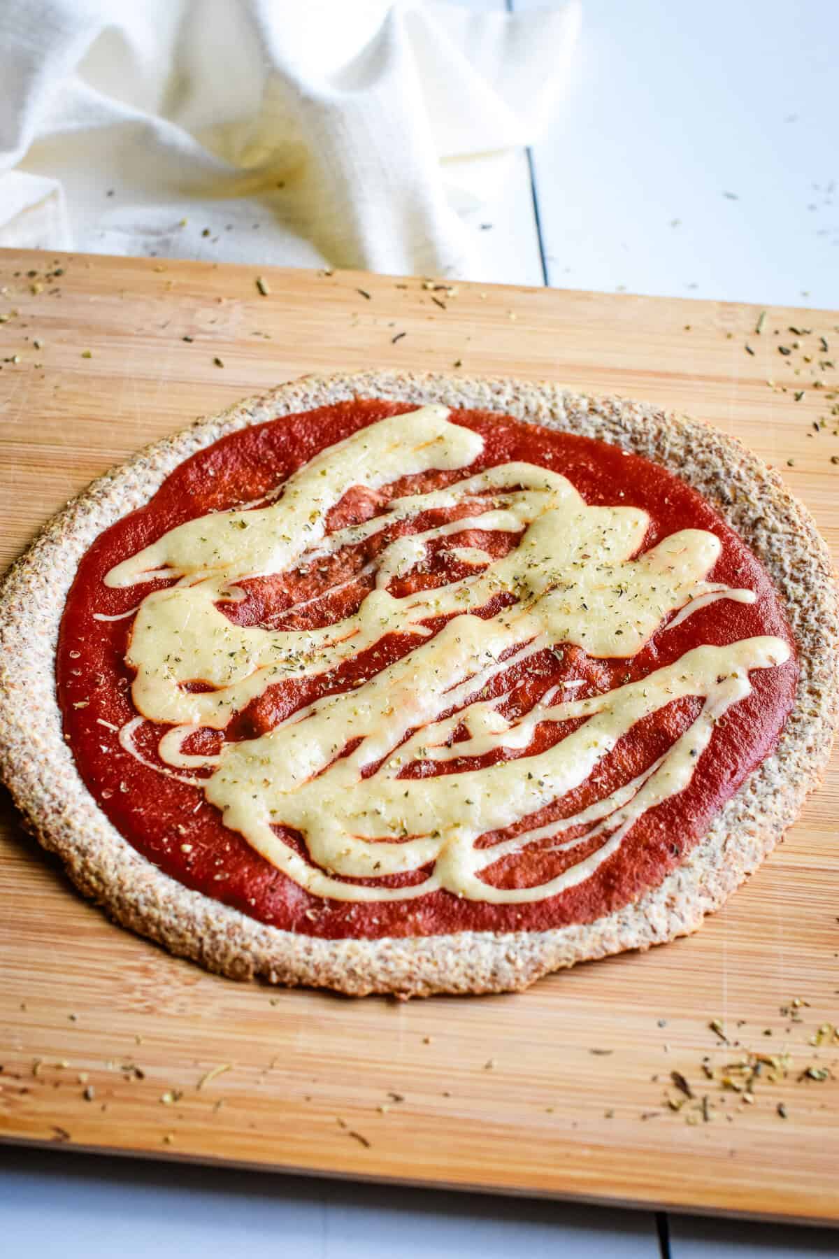 A wooden board with a vegan tortilla pizza on it and Italian seasoning sprinkled around.