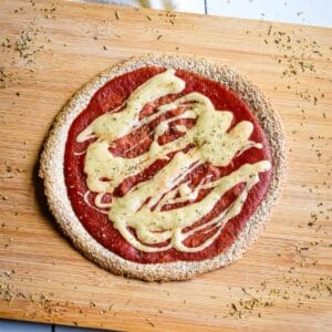 A tortilla with sauce and vegan cheese on a wooden board after baking.