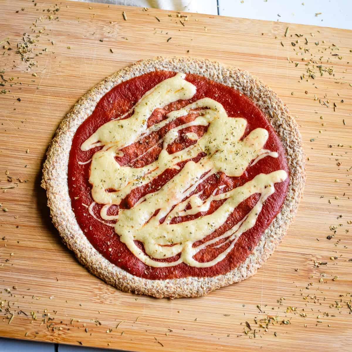 A tortilla with sauce and vegan cheese on a wooden board after baking.