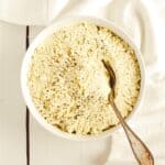 A white bowl filled with tofu ricotta with a spoon in it sitting on a white surface.