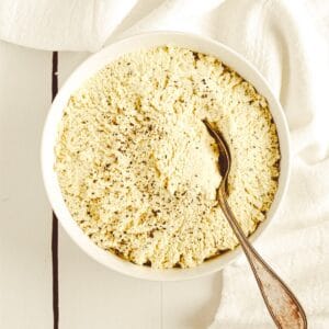 A white bowl filled with tofu ricotta with a spoon in it sitting on a white surface.