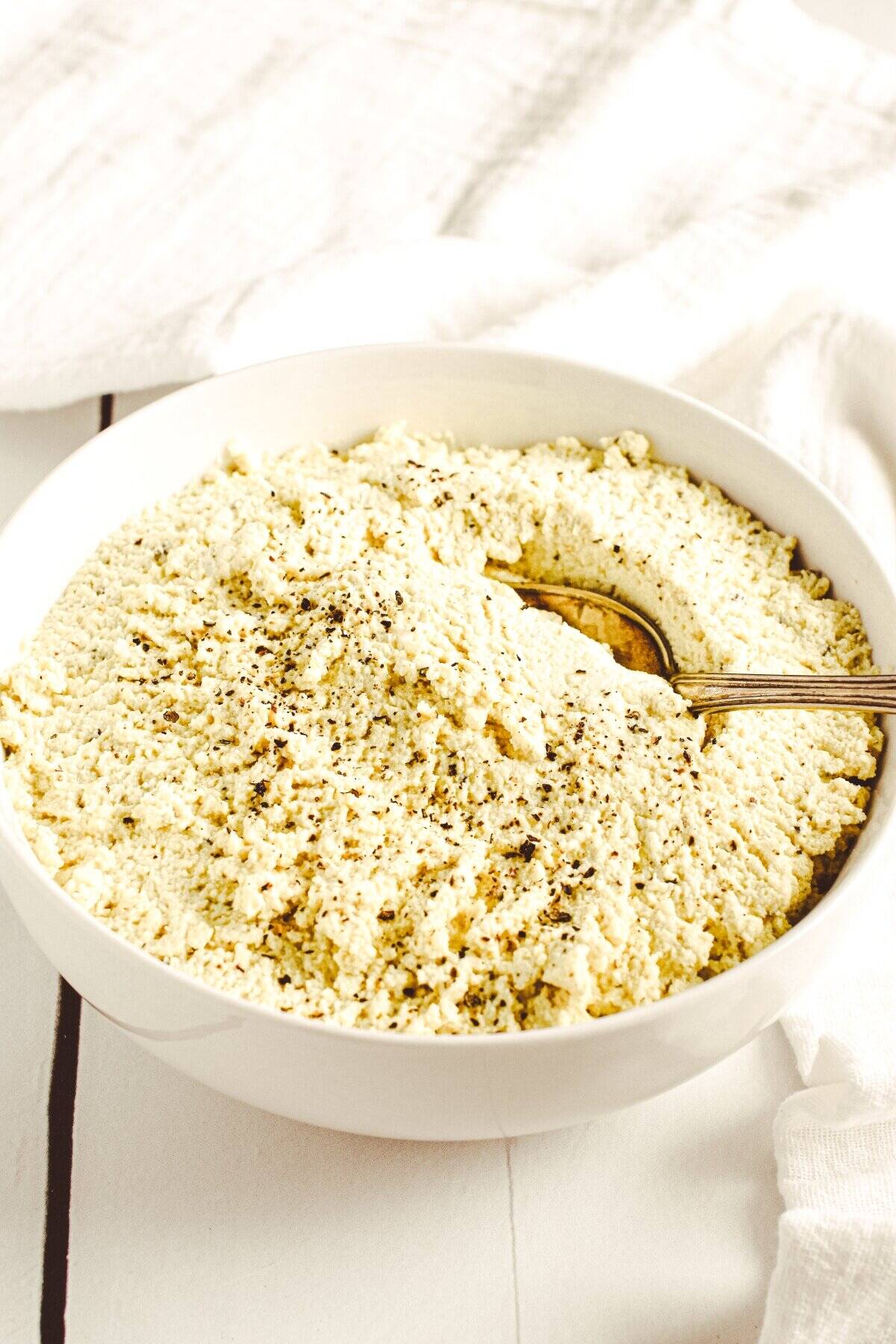 Tofu ricotta in a white bowl with a spoon it it about to scoop some out.